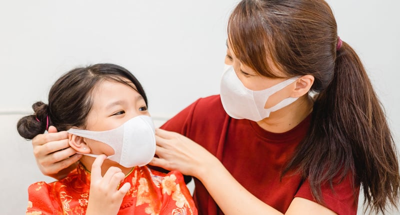 Mom helping her daughter wear a mask to prepare for Chinese New Year.