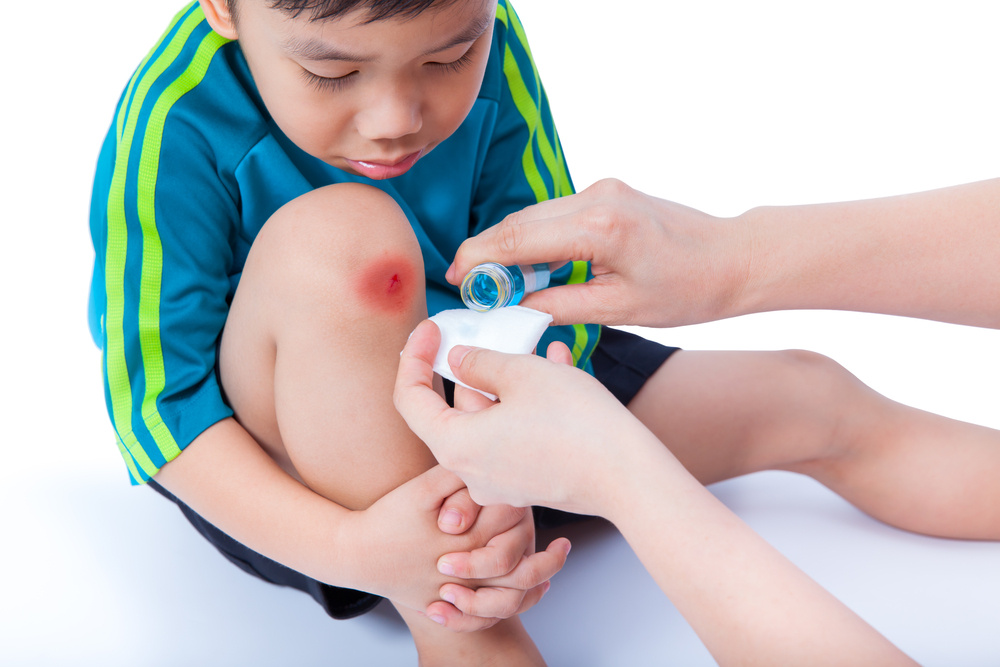 Little asian boy in sportswear looking at his wound, nurse provides first aid