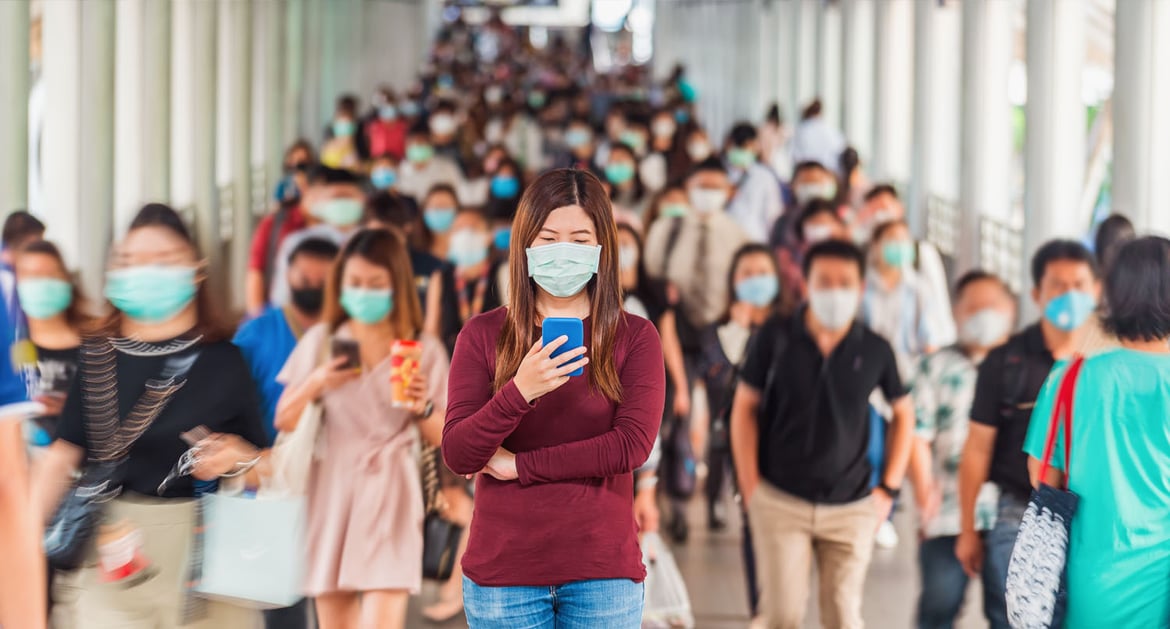 人群中玩手機並佩戴口罩的年輕女性