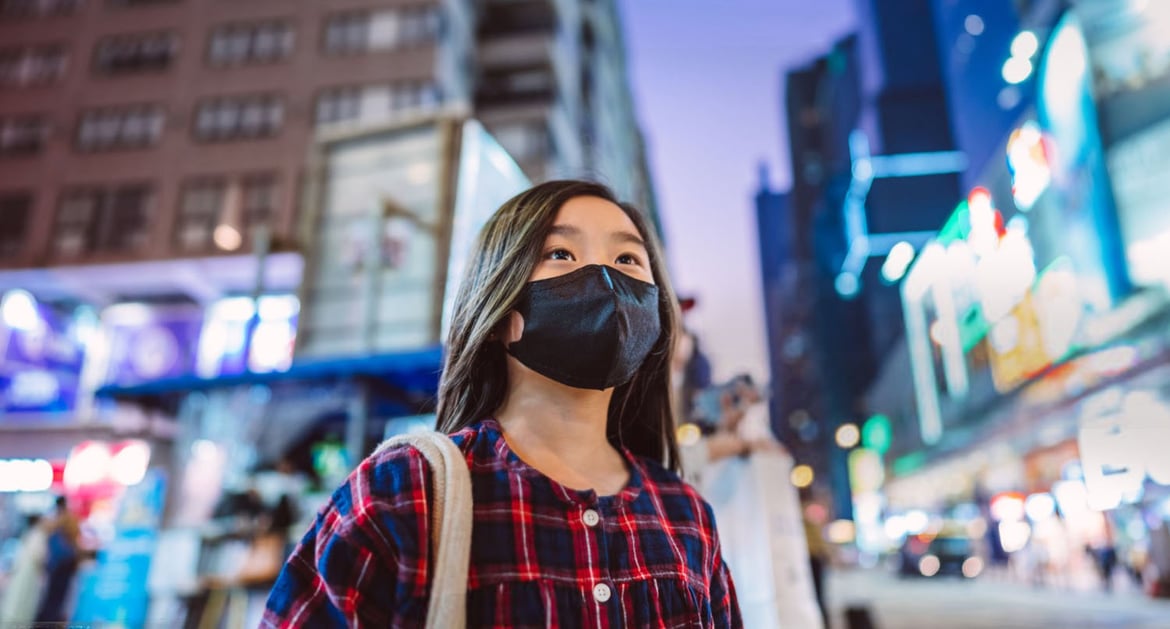A young girl standing in Hong Kong's busy street during Covid looking hopeful.
