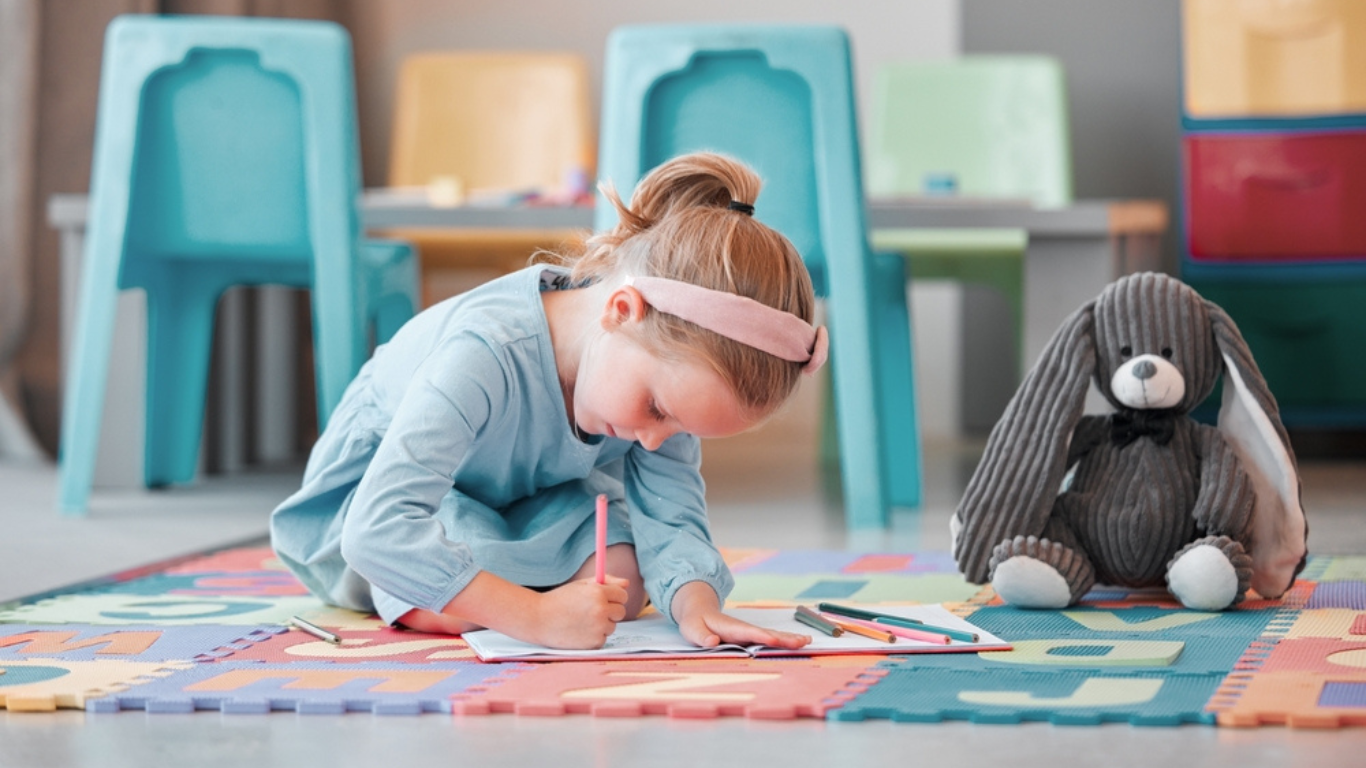 Notebook, teddy bear and young child writing in psychology office for social development. Growth, plush toy and girl kid patient drawing on floor at healthcare clinic for cognitive behavioral therapy