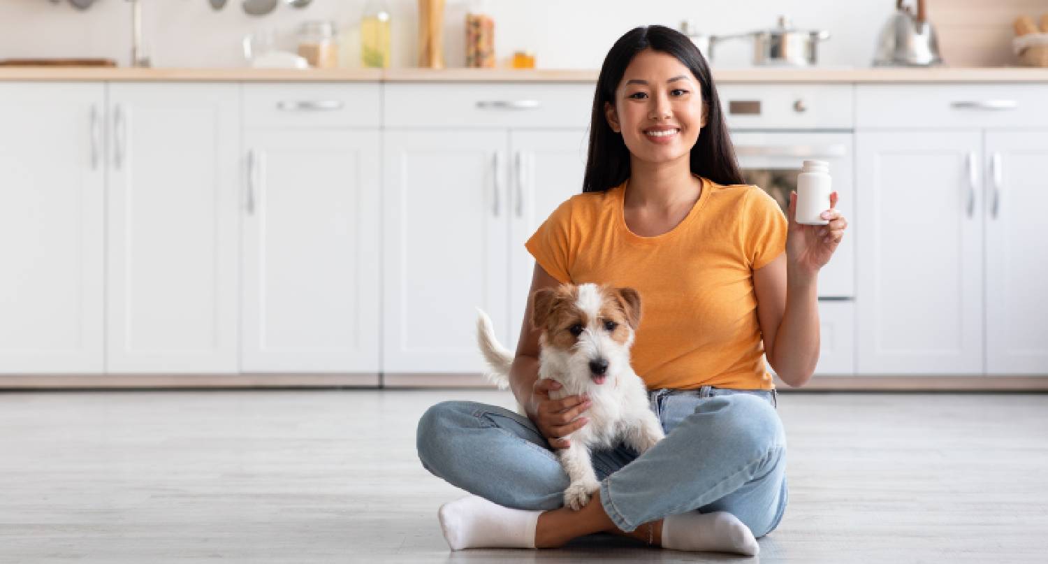 年輕女士抱著小狗和拿著維他命丸坐在地上