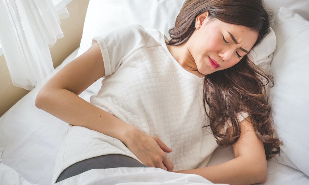 Woman gripping painful stomach on bed