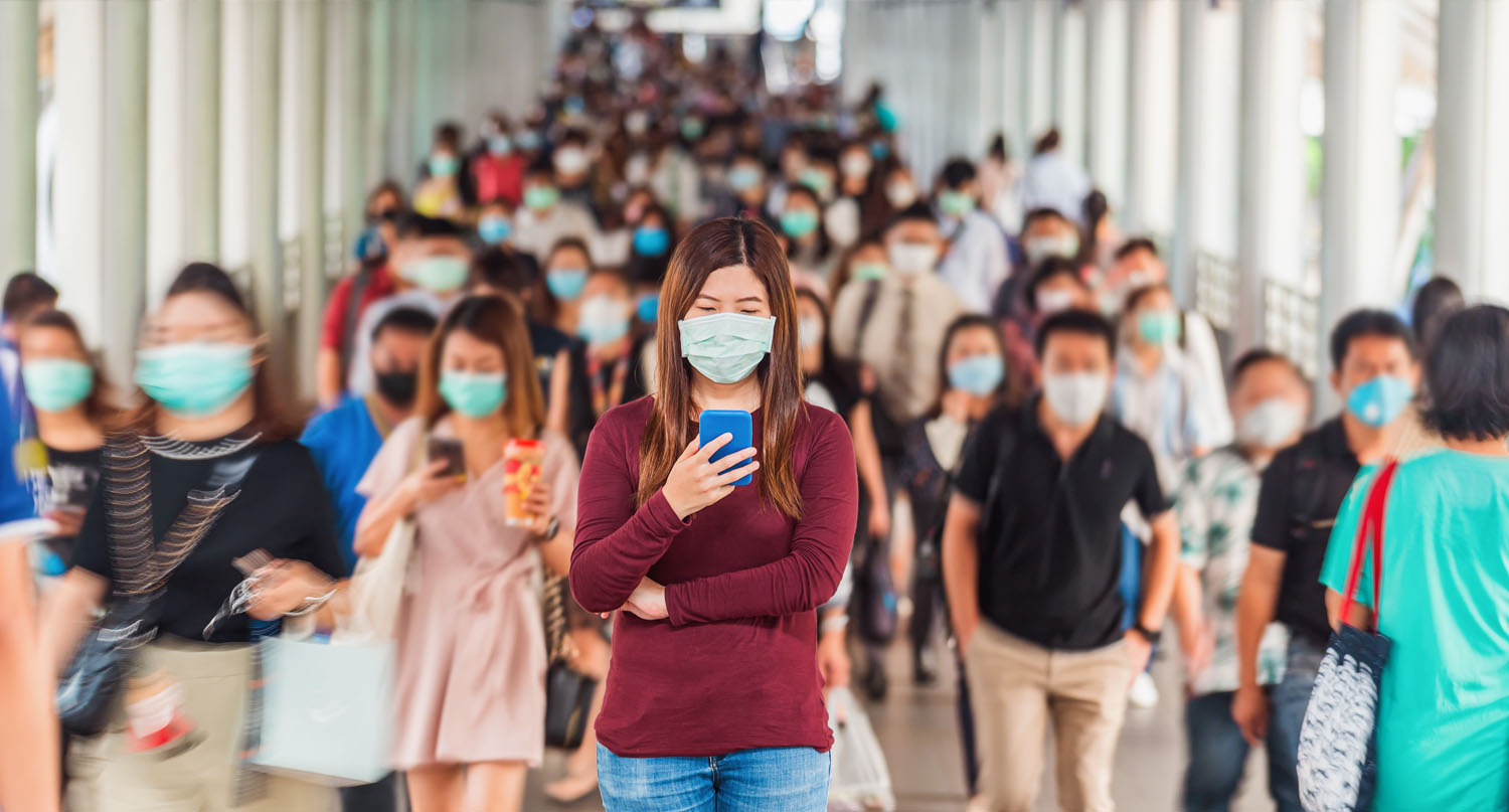 人群中玩手機並佩戴口罩的年輕女性